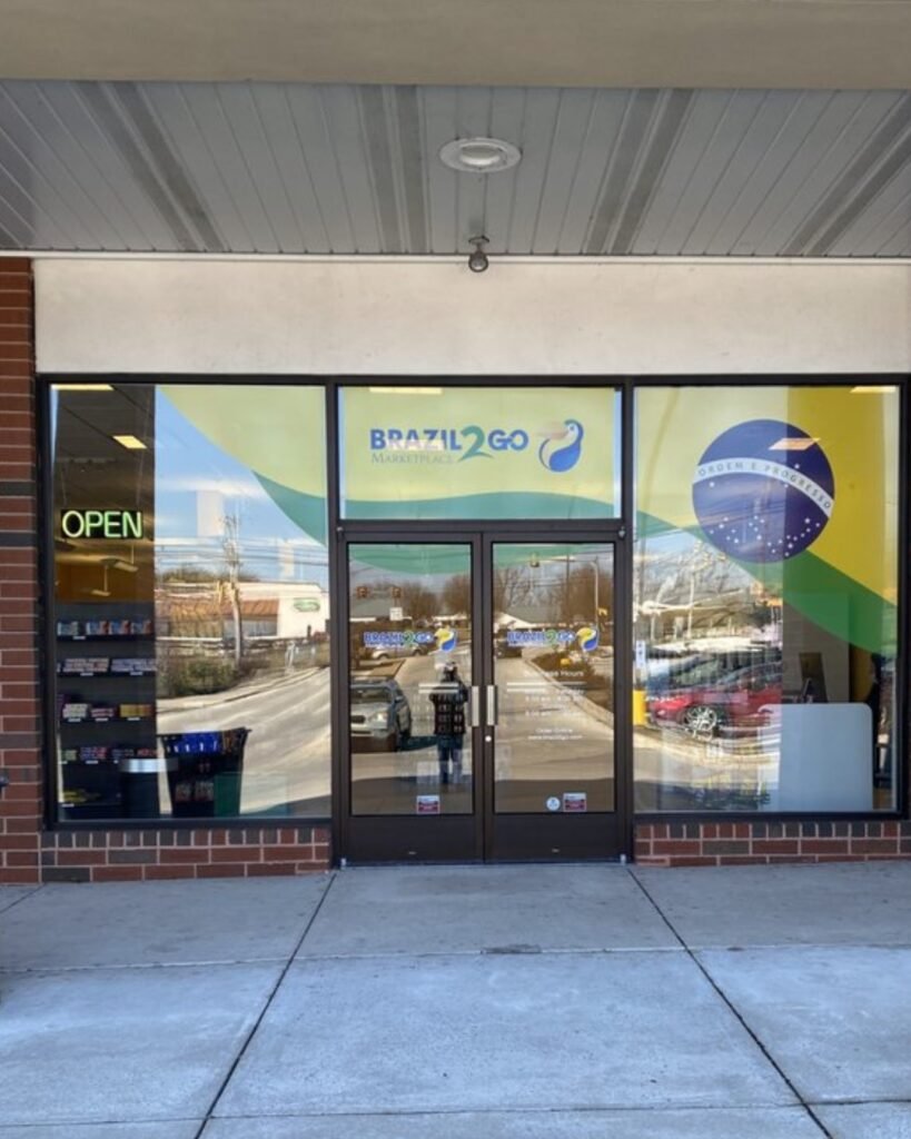 Fachada da loja Brazil2Go Marketplace, com portas de vidro, bandeira do Brasil e placa “OPEN”