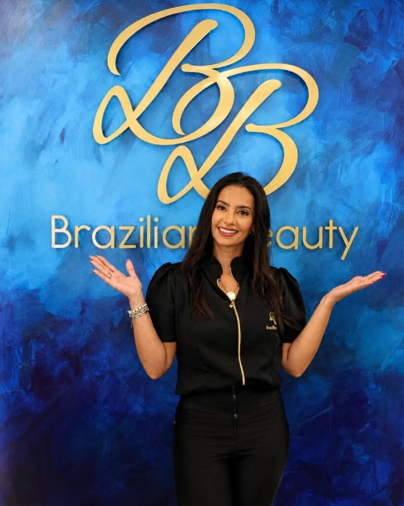 Mulher sorrindo, com os braços erguidos, diante de um painel azul com o logotipo e o texto “Brazilian Beauty”