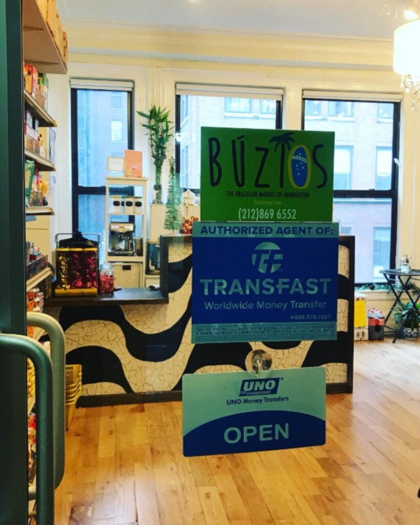 Interior da Buzios NYC, com balcão e placas de serviços de transferência de dinheiro.