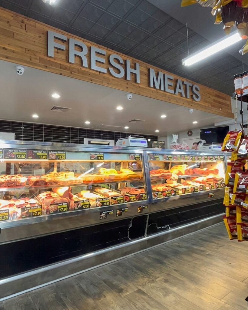 Balcão refrigerado de carnes frescas, com produtos embalados e preços expostos sob a placa “FRESH MEATS”