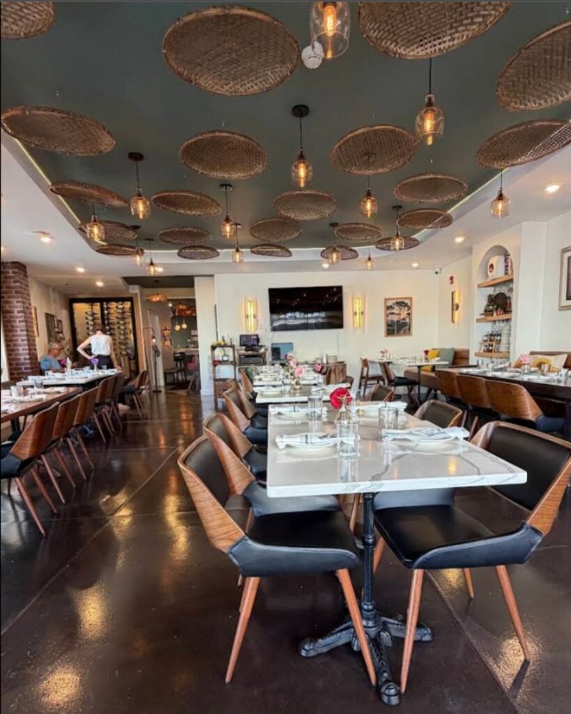 Interior de restaurante com mesas postas, cadeiras de couro e luminárias de vime no teto