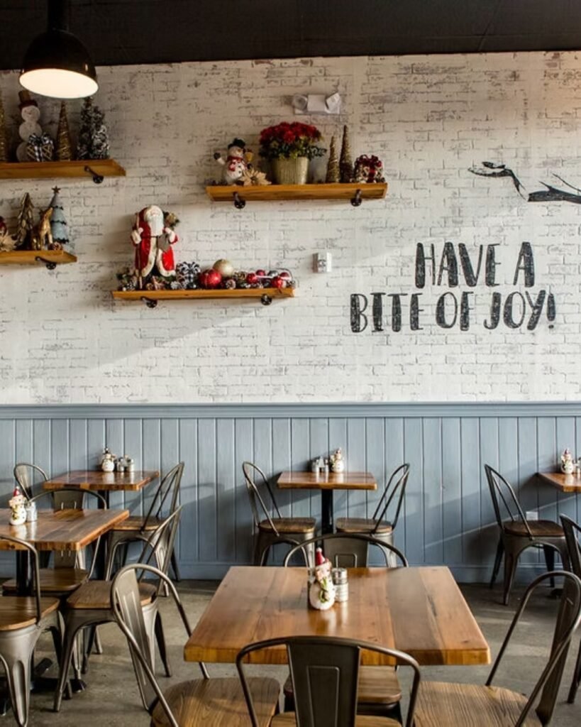 Interior de restaurante com mesas de madeira, decoração natalina e a frase HAVE A BITE OF JOY! na parede
